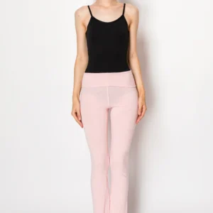 Woman in a black tank top and pink pants standing against a white wall.
