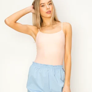 Woman posing in a light pink tank top and blue pants.