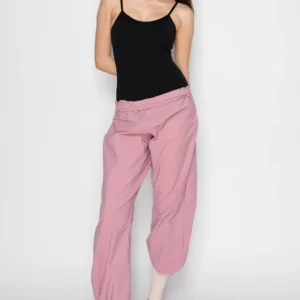 Woman in a black tank top and pink pants posing against a white background.
